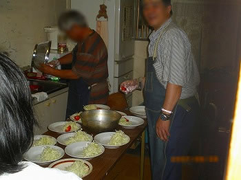台所にて。ボールをふいている人とキャベツの千切りが入った皿に盛りつけている人
